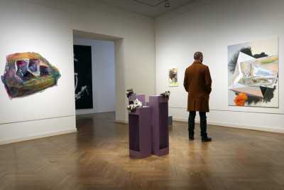 Besucher betrachtet ein Bild von der Künstlerin Maja Rohwetter, Außerdem im Raum sind kleine Keramik Skulpturen in der Mitte des Raums und ein buntes Kunstobjekt an der Wand.