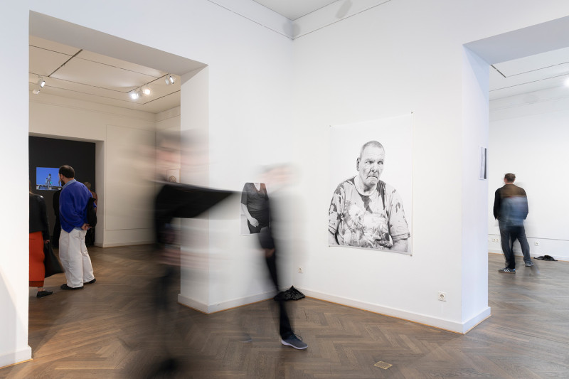 text: >
  Besucher laufen durch die Galerieräume.
  An einer Wand hängt eine
  Porträtfotografie eines Mannes
decorative: false
source: reviewed