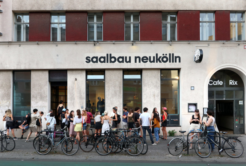 Exterior view of the gallery in the Saalbau. People are standing in front of it, dressed in summer clothes and talking to each other.