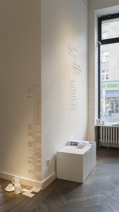 View of the room, there is writing on the walls and notes stuck to the corner of the wall, there are cups on the floor in front of it.