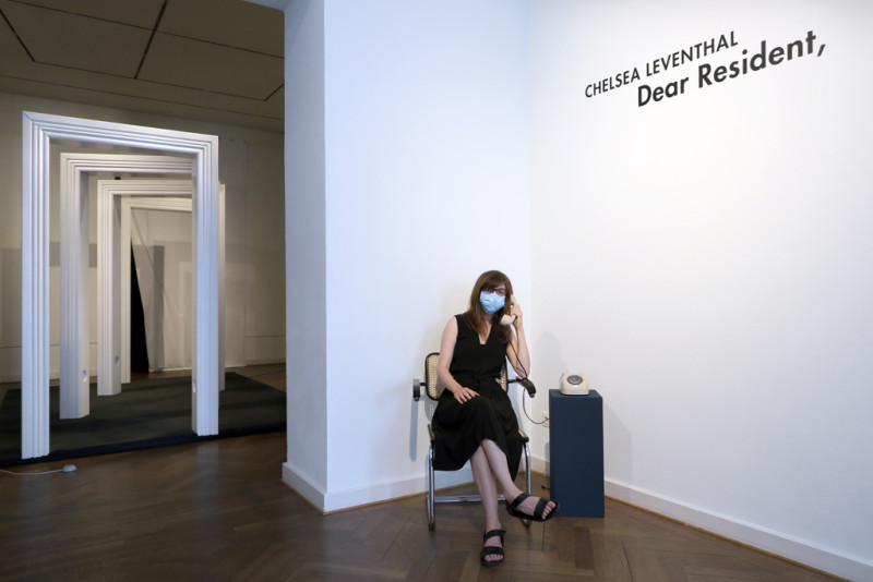 die Künstlerin lauscht den Geräuschen aus einem  beigen Drehscheibentelefon