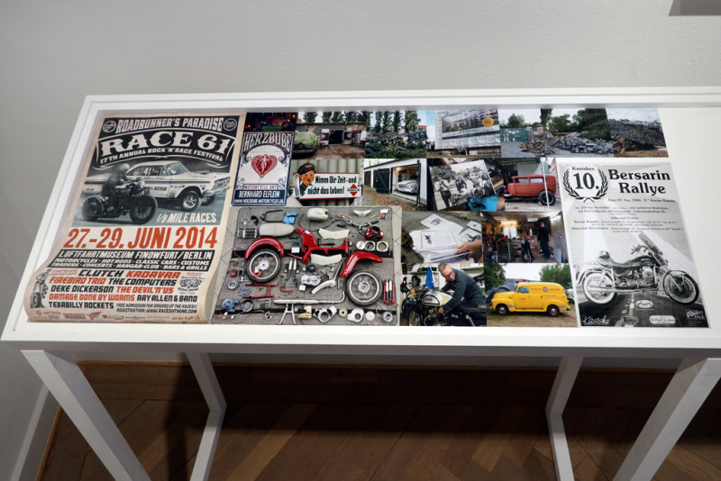 Display case with photos and posters of cars and motorbikes.