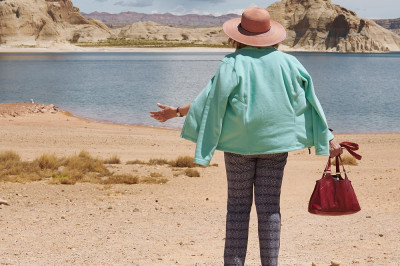 Eine Frau steht an einem See in der Wüste und streckt die Arme aus.