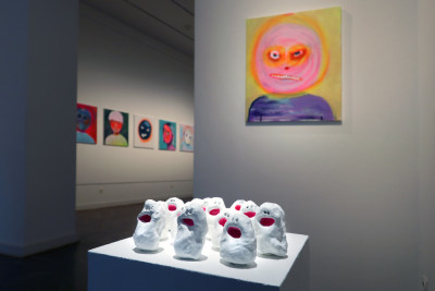 Pictures with emotional faces hang on the walls. In the foregreound, small figures with open red mouths stand on a pedestal.