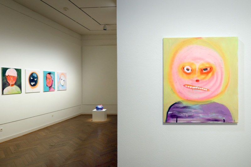 Blick durch die Räumlichkeiten. Ein Bild mit einem wütenden Gesicht im Vordergrund. Im hinteren Raum hängen noch weitere Bilder.