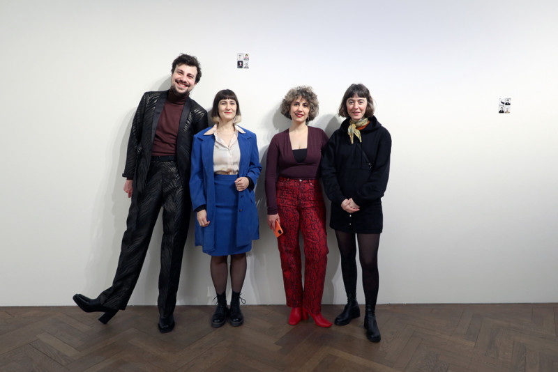 The four artists of the exhibition stand smiling in front of a white wall.