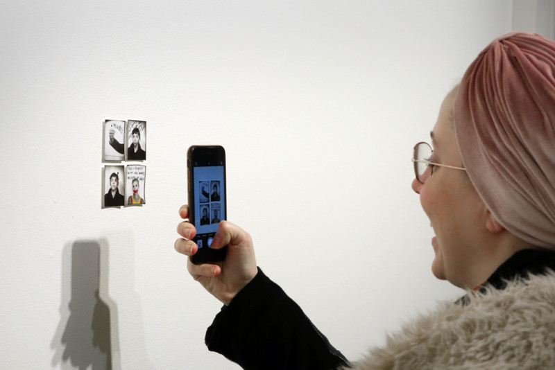 A visitor takes a photo of four small passport fotos on the wall.