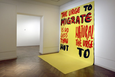 View into the room. Large yellow poster, with red and black lettering: 