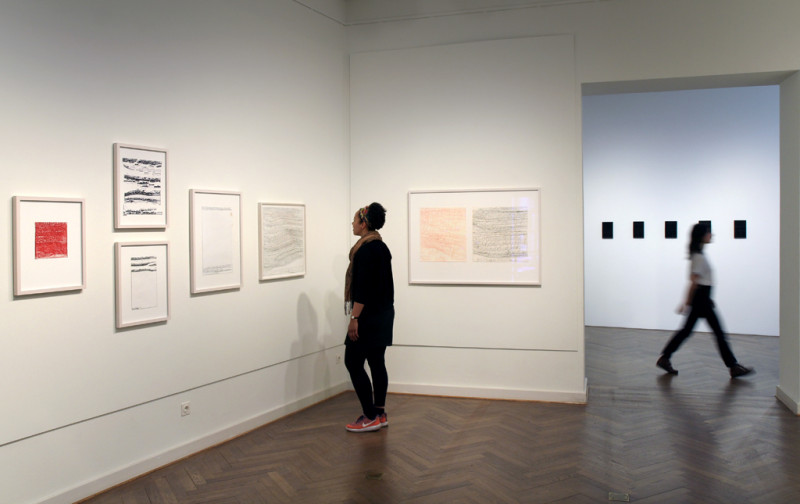 Eine Besucherin betrachtet Zeichnungen von Harald Stoffers. Eine weitere Besucherin bewegt sich in dem Raum mit den Werken von Etienne Dietzel.