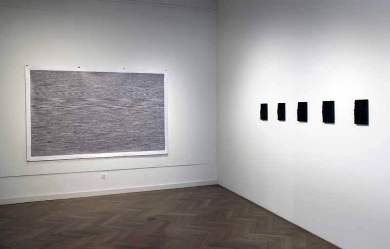 An der linken Wand hängt ein großer abstrakter Schwarz-Weiß-Print. An der rechten Wand sieht man fünf kleine schwarze 3D-Drucke.