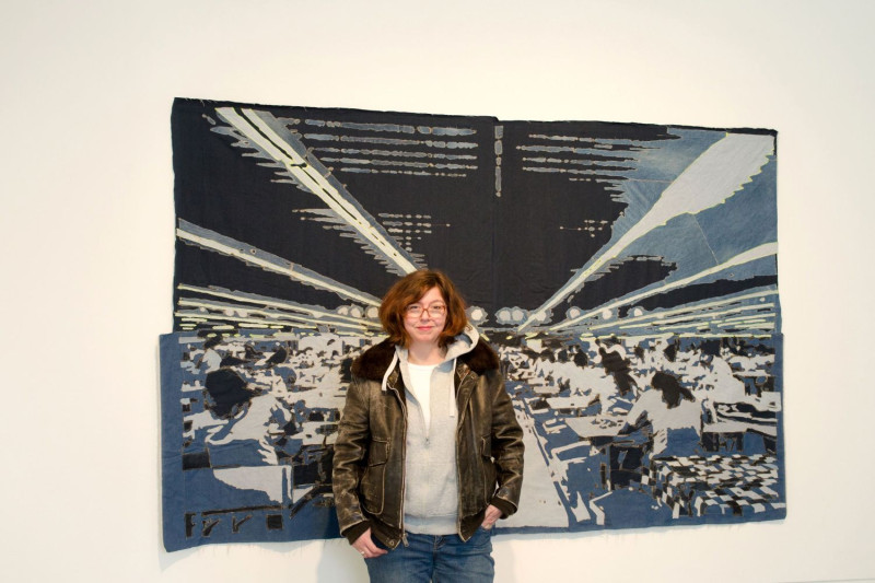 Die Künstlerin Katrin Hoffert steht vor ihrem genähten Jeansbild.