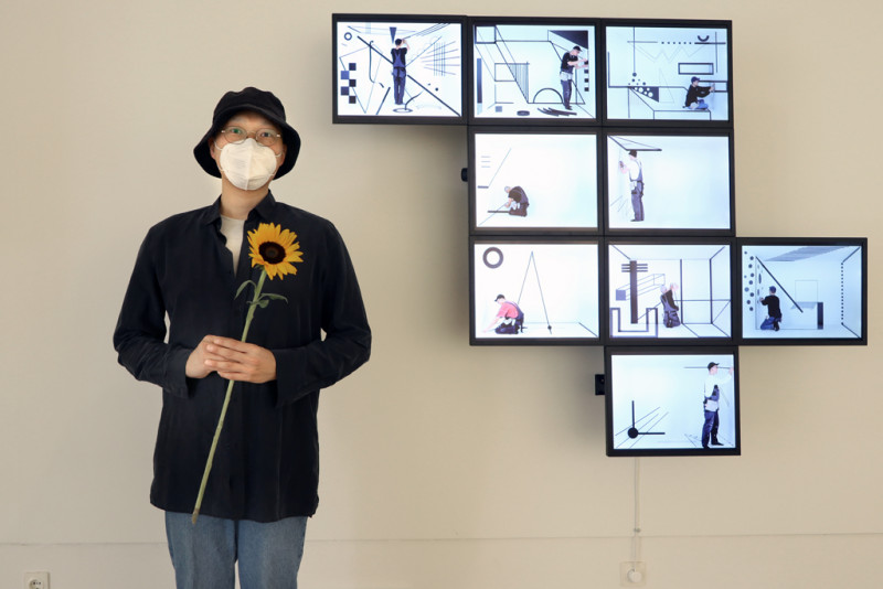 Hyunho Park: vor ihrem Objekt: Time Crystals -  Neun Räume, 2019. Auf der rechten Seite des Bildes hängen 9 Monitore an der Wand.