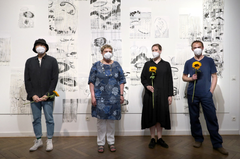 Die Stadträtin Karin Korte steht mit den 3 Preisträgier:innen vor einer schwarz weißen Papierarbeit an der Wand in der Galerie.