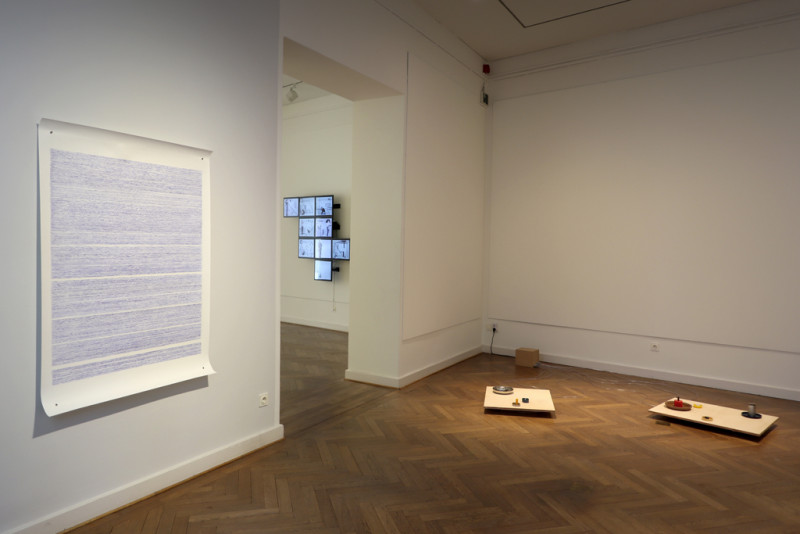 an der rechten Wand hängt eine großformatige Papierarbeit mit blauen Wellenlinien und am Boden auf der rechten Seite steht eine Arbeit, die aus vielen Kleinen schüsseln mit Wasser besteht