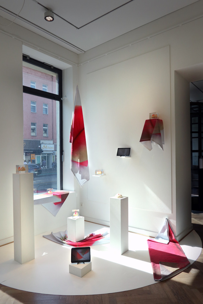 Auf weißem Grund stehen weiße Sockel mit rosa decken und kleine Skulpturen drauf. Die Installation ist vor dem Fenster der Galerie