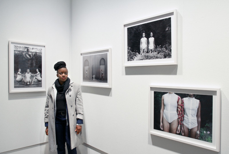 Die Künstlerin Médine Tidou steht vor ihrer Fotografieserie. Schwarz weiß Fotos in schwarzen Rahmen zeigen Frauen im Körnerpark.