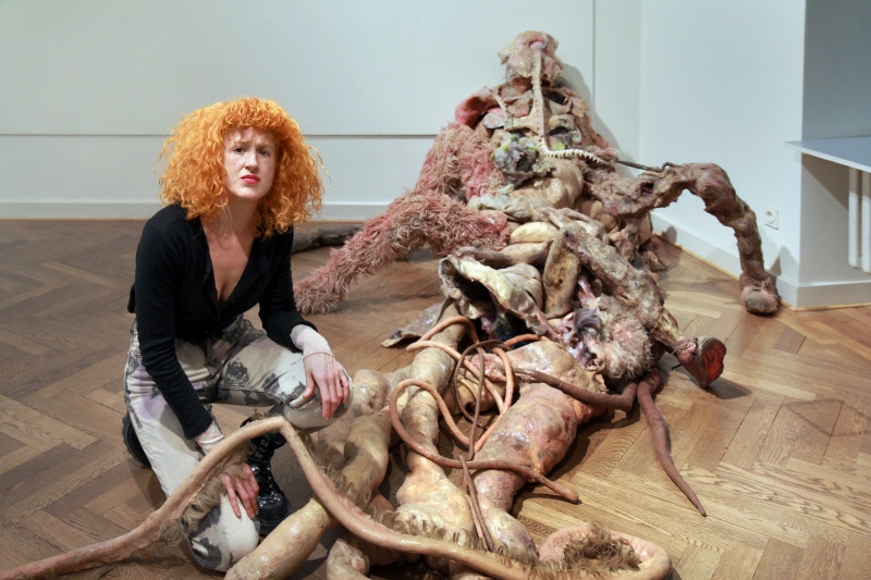 Die Künstlerin hockt auf dem Boden vor einer großen Skulptur aus fleischigem Silikon.