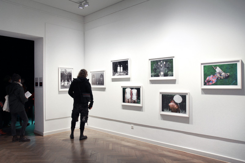 Besucher:innen stehen vor einer Wand mit weiß-gerahmten schwarz-weiß Fotografien.