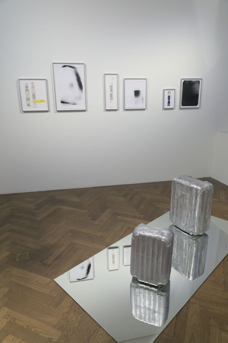 On the floor is a mirror with two aluminum casts in the shape of suitcases. Pictures of various sizes hang in the background