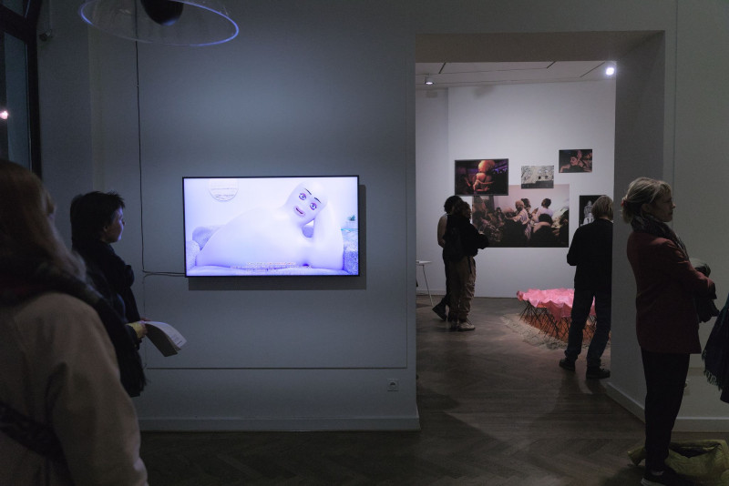 The picture shows a screen with video work and visitors at the vernissage