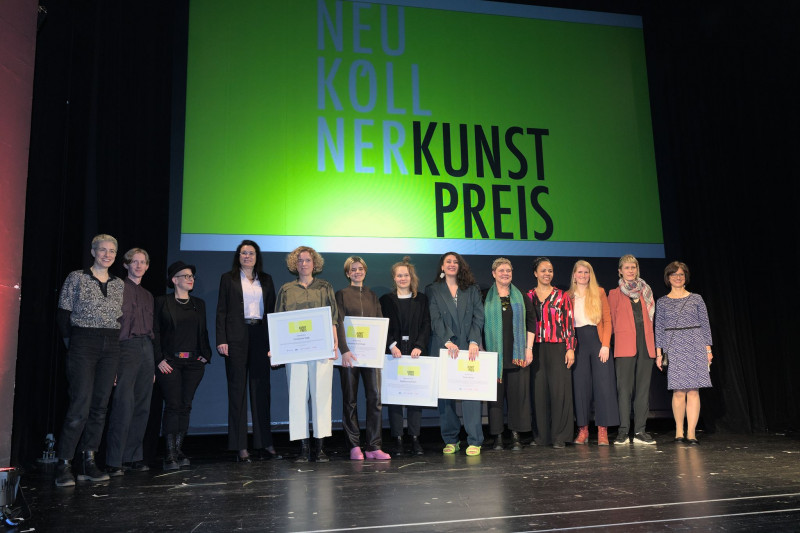 The award winners stand on the stage of Heimathafen Neukölln together with the jury and the city councillor for culture