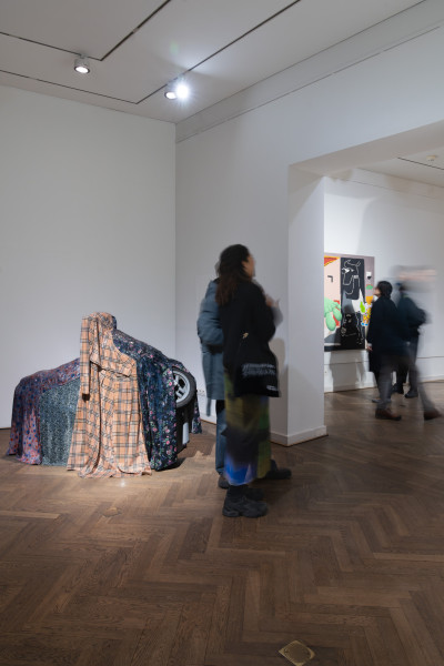 Man sieht den Eingangsbereich der Galerie, links steht eine Skulptur. Es handelt sich um ein Motorrad mit Textilien darüber.