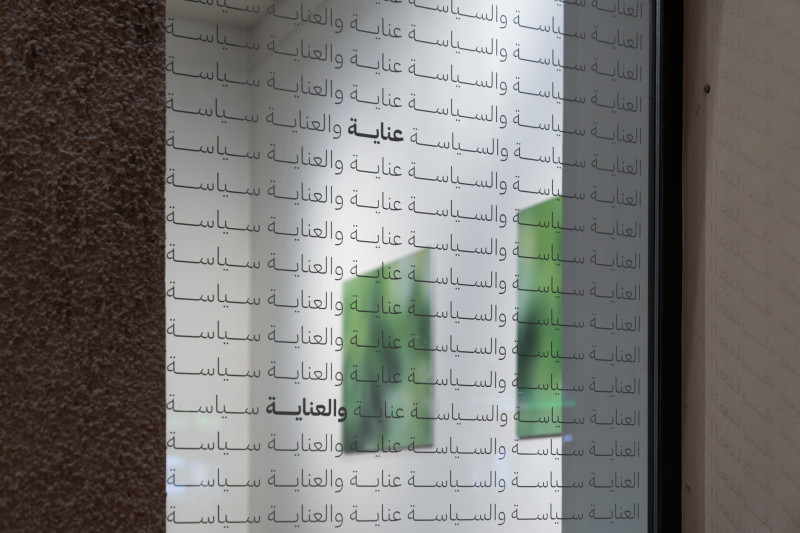 Man sieht ein Fenster der Galerie mit arabischen Schriftzug drauf, im Hintergrund in der Galerie sind zwei grüne Fotografien zu erkennen.