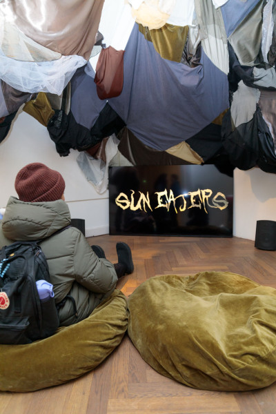 A visitor sits on a green cushion and watches the video of Maryna Makarenko's work “Sun Eaters.”