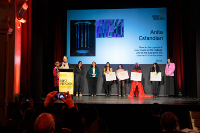 Several people are standing on a stage. The winners of the art prize are holding their awards in their hands.