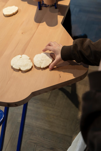 Person's hand hovering over white cookie on a wooden surface in an art space