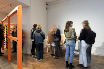Visitors exploring an art exhibition with wooden structural elements and blurred figures moving through the gallery space