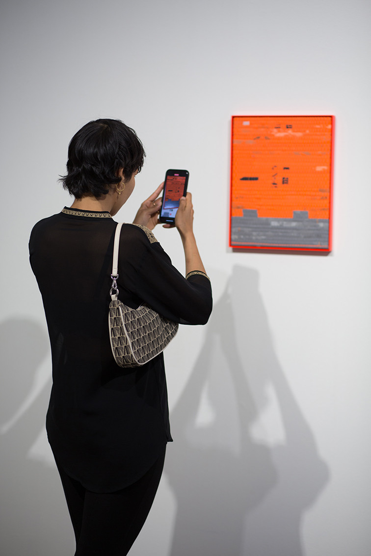 A person stands in front of a wall piece woven from neon-orange fabric.