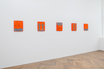 Neon-orange weavings hang on a wall