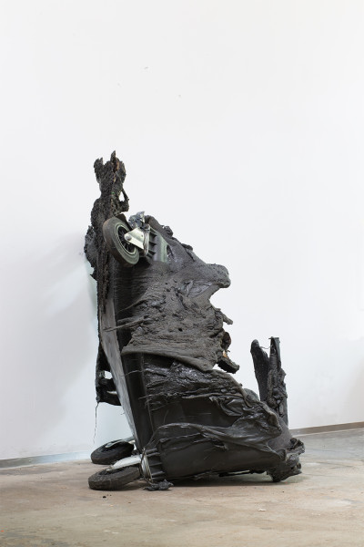 A burnt garbage can stands in front of a white background