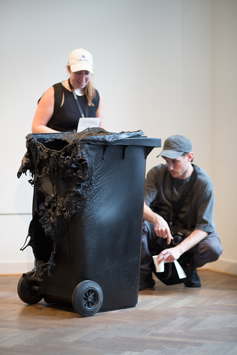 Two people looking at a burnt black trashbin