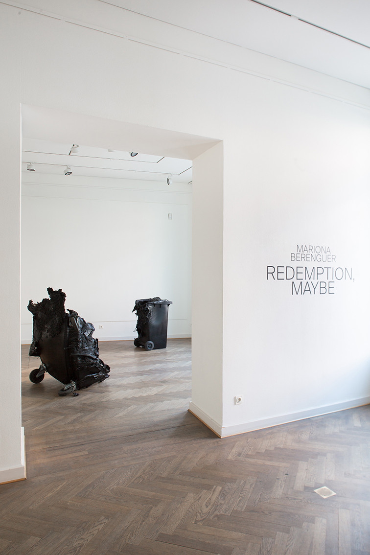 The title of the exhibition and two burnt black Trashbins can be seen