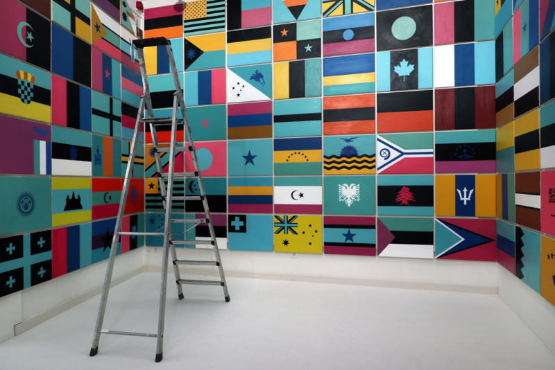 Der Galerieraum wird von der Decke bis zum Boden von farblich invertierten Staatsflaggen bedeckt.