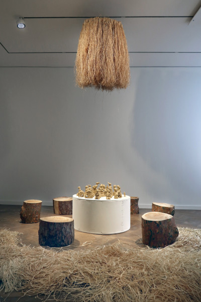 Sitzgelegenheiten aus Baumstämmen mit einem weißen Sockel in der Mitte und Figuren auf Lehm