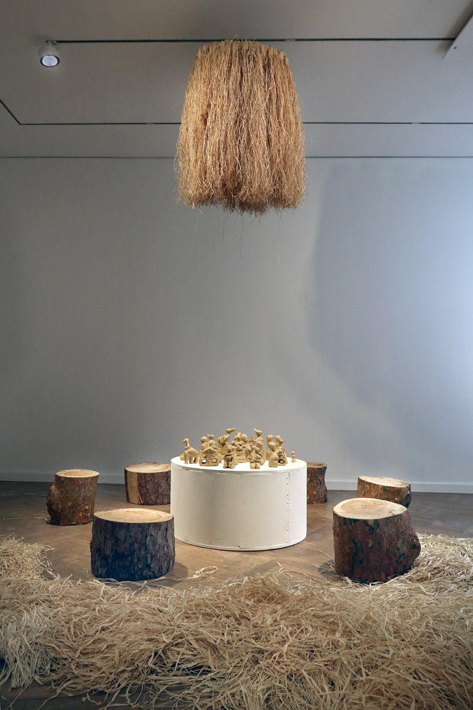 Sitzgelegenheiten aus Baumstämmen mit einem weißen Sockel in der Mitte und Figuren auf Lehm