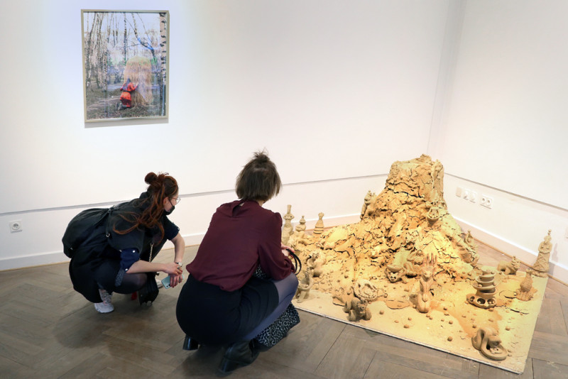 Eine Fotografie auf der Viviana Druga bei ihrer Performance im Wald zu sehen ist und ein Vulkan auf Lehm