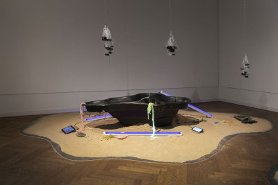 Three neon tubes with black light lie on a pile of sand next to a garden pond bowl and several Ipads with video works.