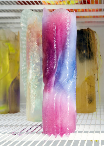 Detailed view of a refrigerator containing frozen neon-colored objects made of fabric and artificial hair.