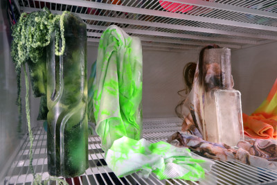 Detailed view of a refrigerator containing frozen neon-colored objects made of fabric and artificial hair.