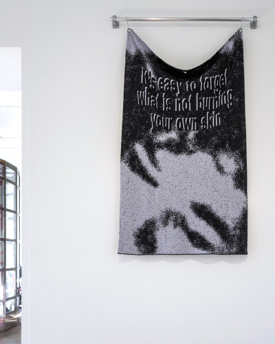 A merino wool blanket hangs on the wall with the inscription ‘It's easy to forget what doesn't burn your own skin’.