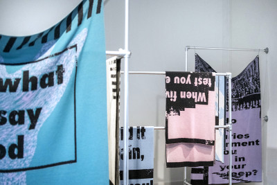Merino wool blankets in various colours printed with text hang on a metal frame.