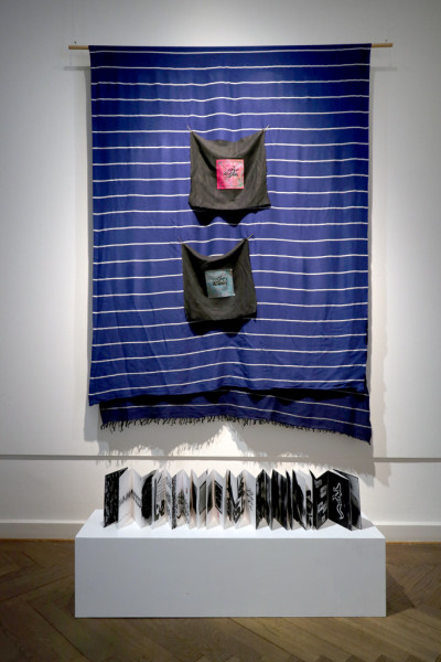 Textil mit zwei arabischen Schriftzeichen mit ausgebreitetem Buch davor