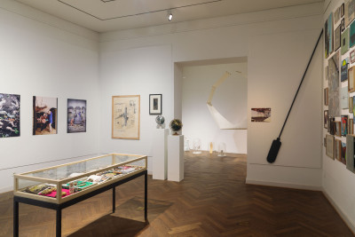 Interior view of the Galerie im Saalbau. On display are a display case and several works of art hanging on the wall, as well as a view into a gallery room behind it.