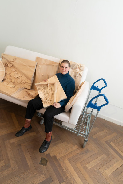 Künstlerin Cornelia Herfurtner sitzt auf weißem Sofa umgeben von ihren Holzarbeiten.