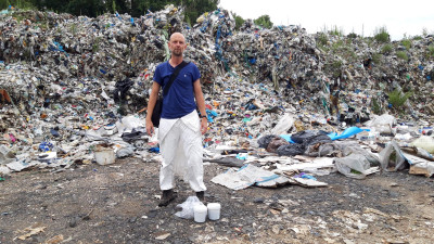 A man stands among piles of garbage.